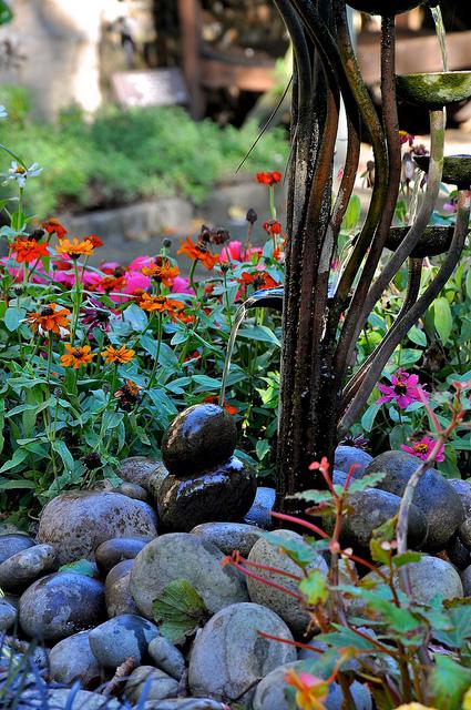 RIver rock and brightly colored flowers surround a metal water feature